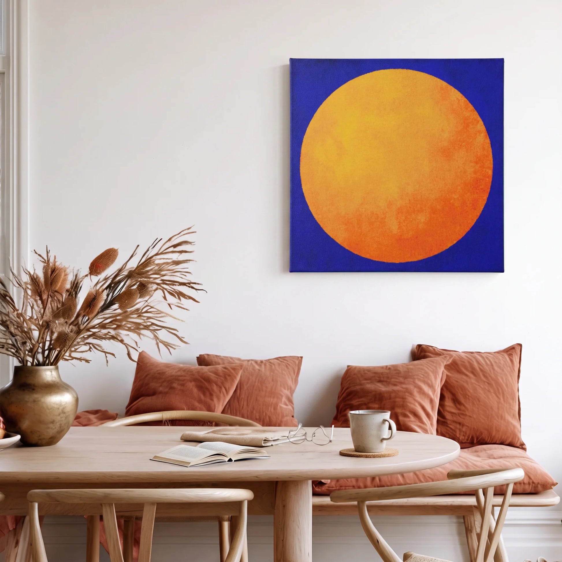 Uplifting wall art sun canvas in warm dining area with terracotta cushions and dried florals